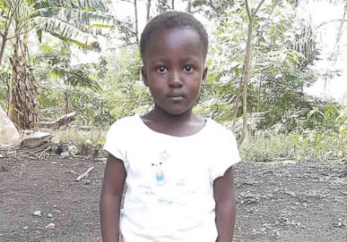 A little girl in white stands looking at the camera